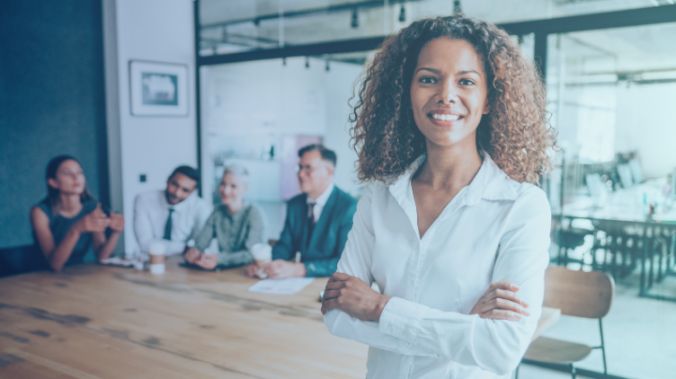 A women smiling crosshanded with people at work discussing in the background