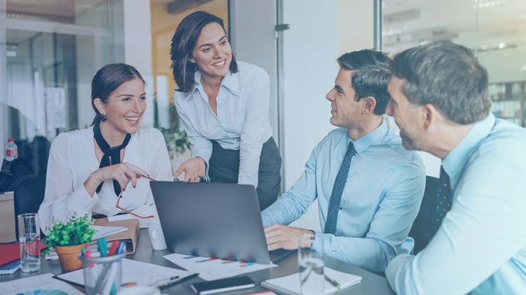 4 people talking happily at a desk with open laptop