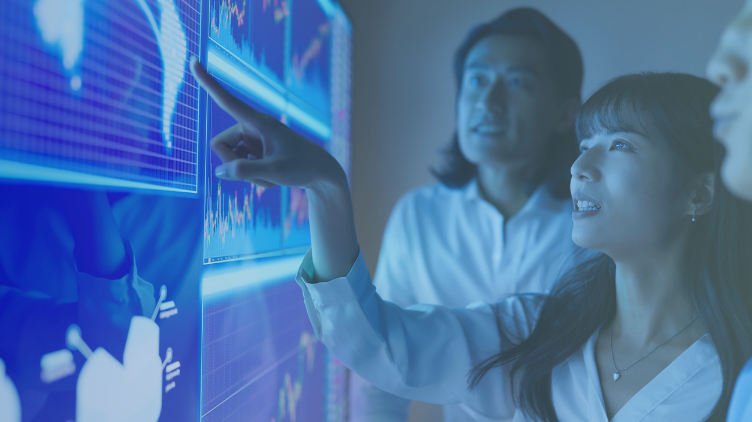 A woman points at data charts on a large digital screen while colleagues look on.